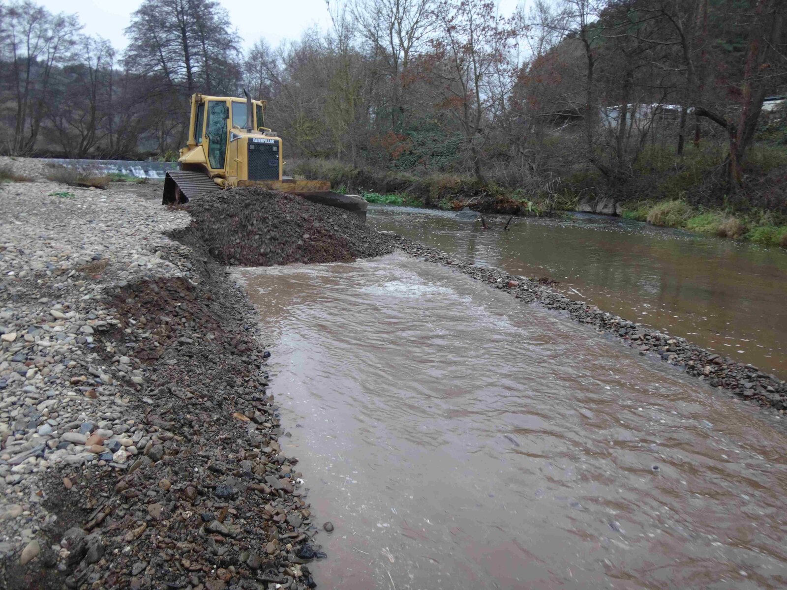 Abschieben von Kiesbänken vom Unterwasser eines Wehres bis unterhalb einer flussabwärts stehenden Brücke mittels einer Raupe.